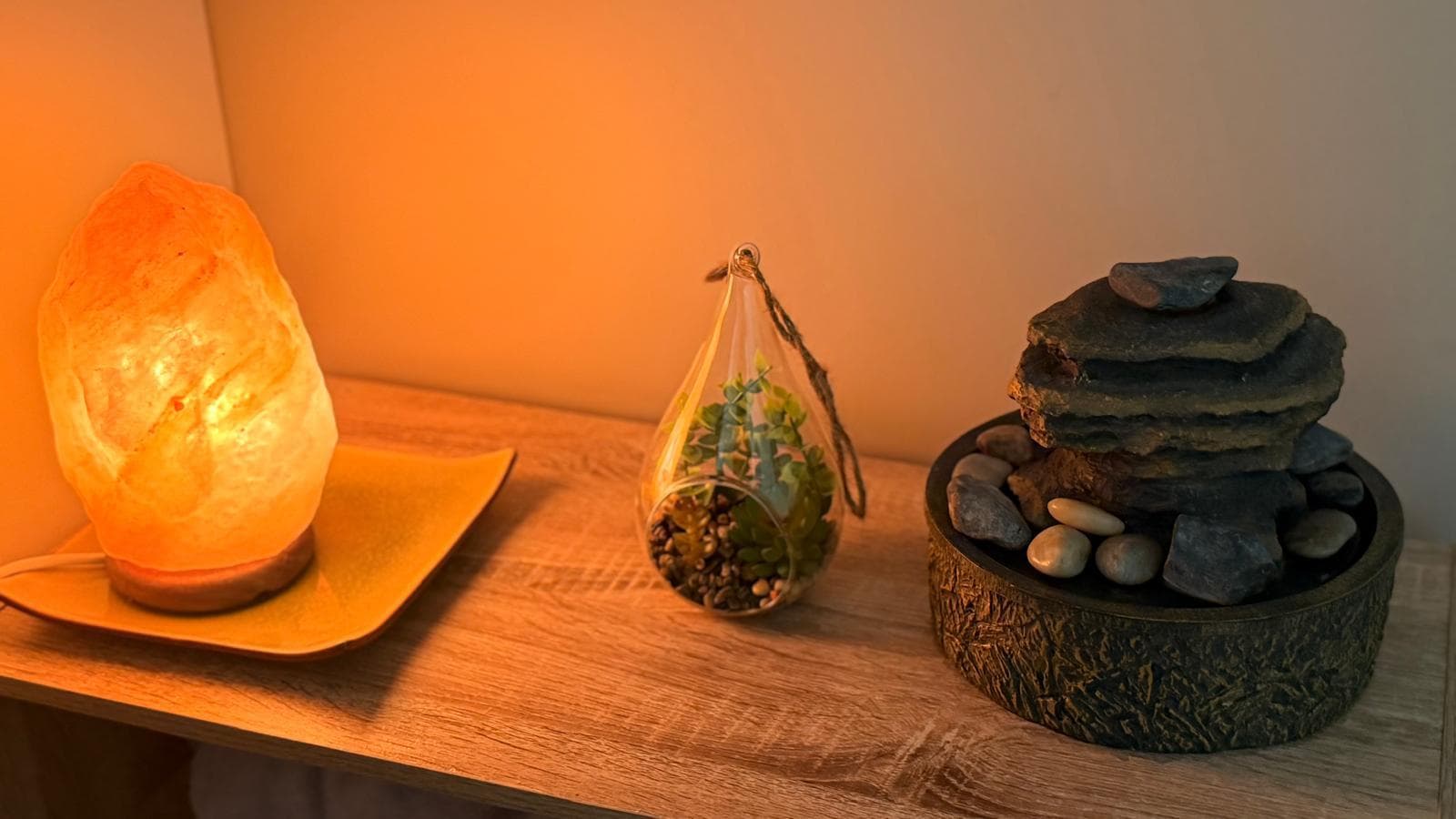 Lampe de sel allumée, terrarium suspendu et fontaine de galets sur une étagère